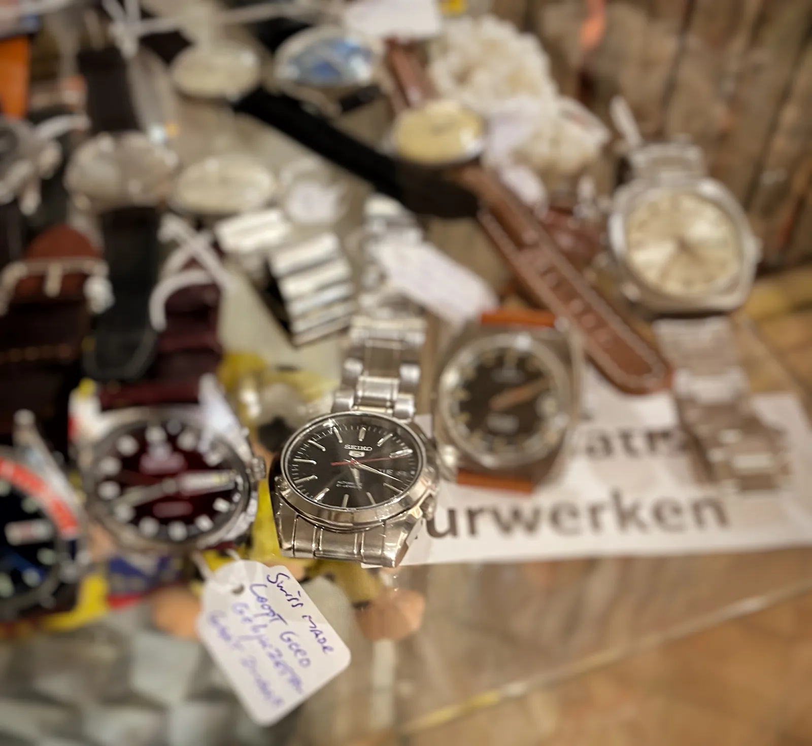 Many wrist watches on display here. Just one of them is clearly in focus. It points at 18 minutes past 5.