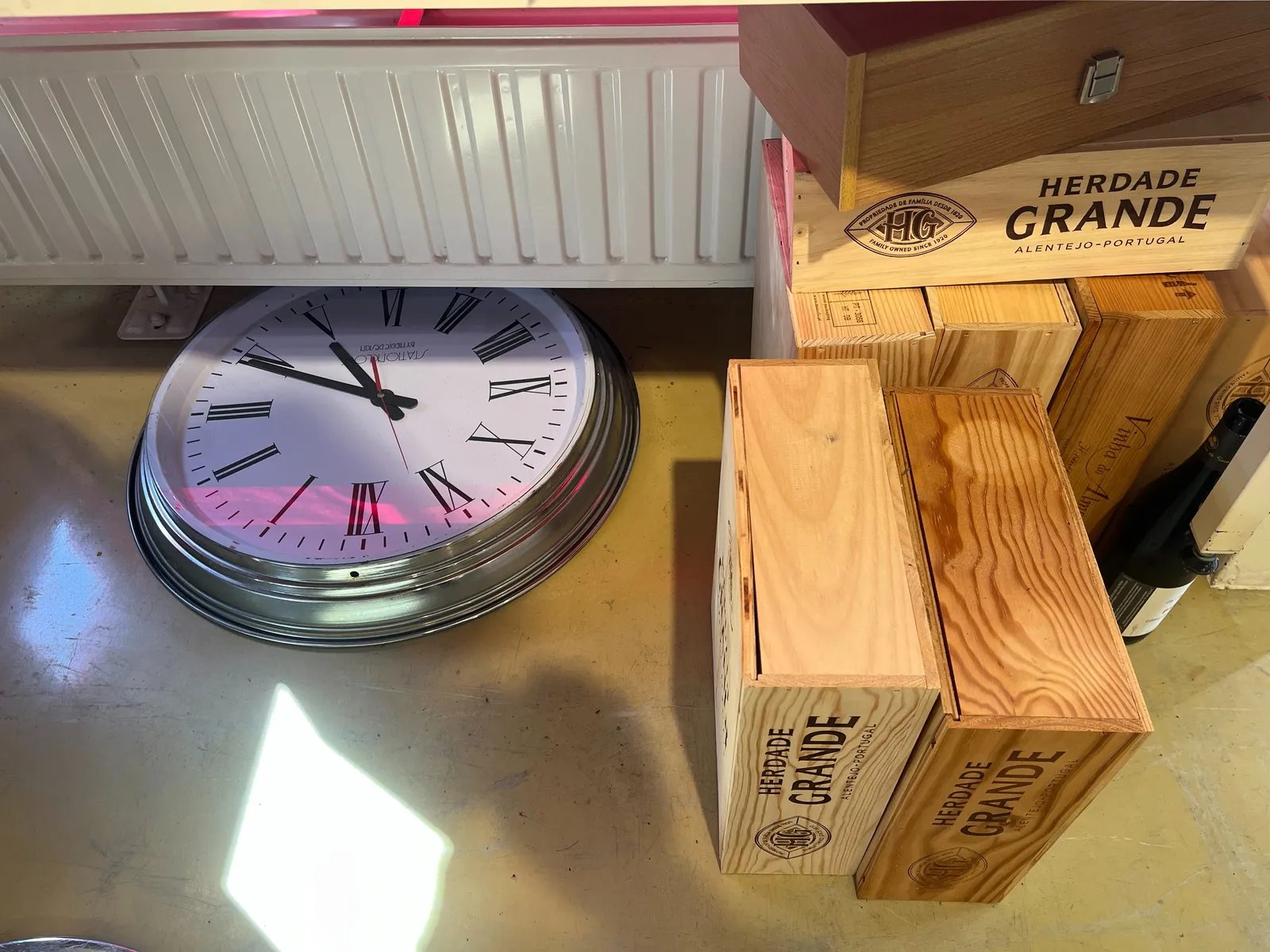 On the floor, next to quite a few wooden wine crates, lays a clock, under a radiator. It’s a bit off, so it either points at 19 minutes past 4, or at 19 minutes past five