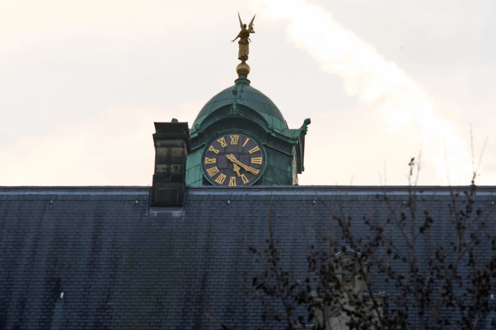 Behind a huge roof there’s a tower with a clock on it. It points at 20 past 5.