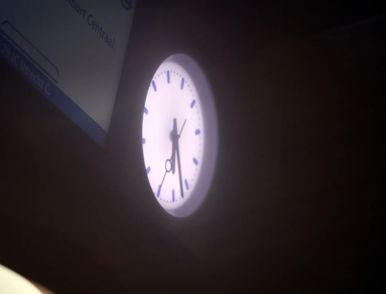 A lit clock surrounded by blurry darkness. It points at 22 minutes past 5.