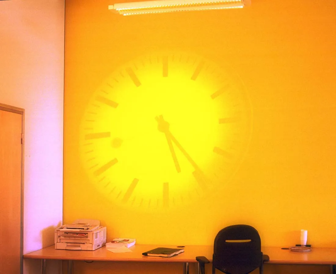 A projection of a clock on a yellow wall shows us that it is five twenty four.