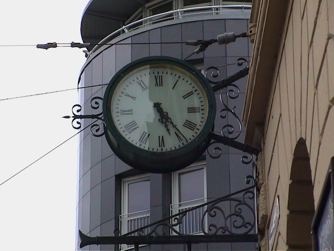 A clock hanging from a facade points at twenty four past five.