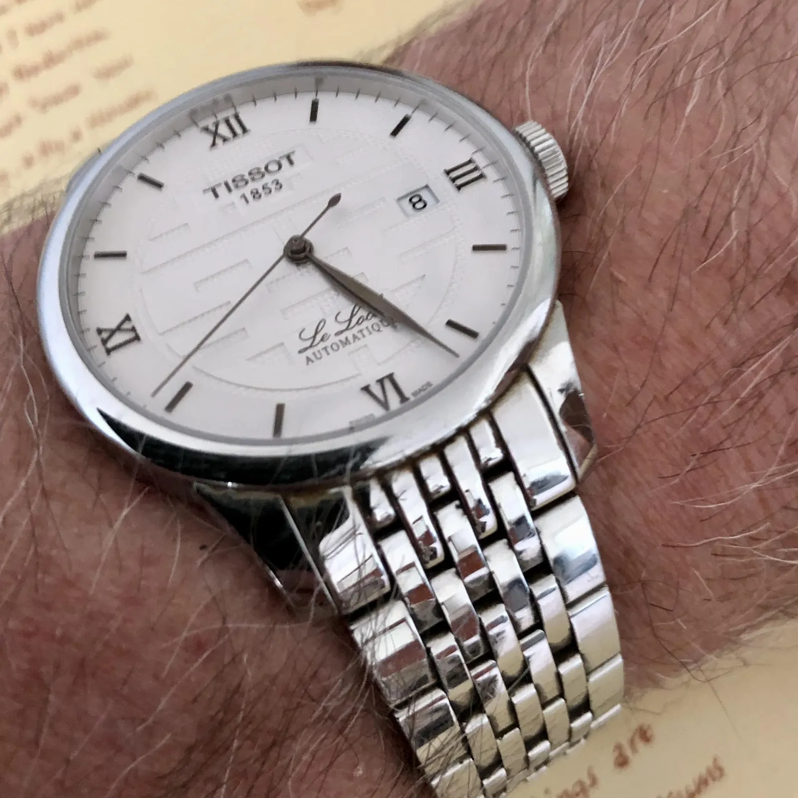 A shiny wrist watch on a wrist. It points at 26 past 5.