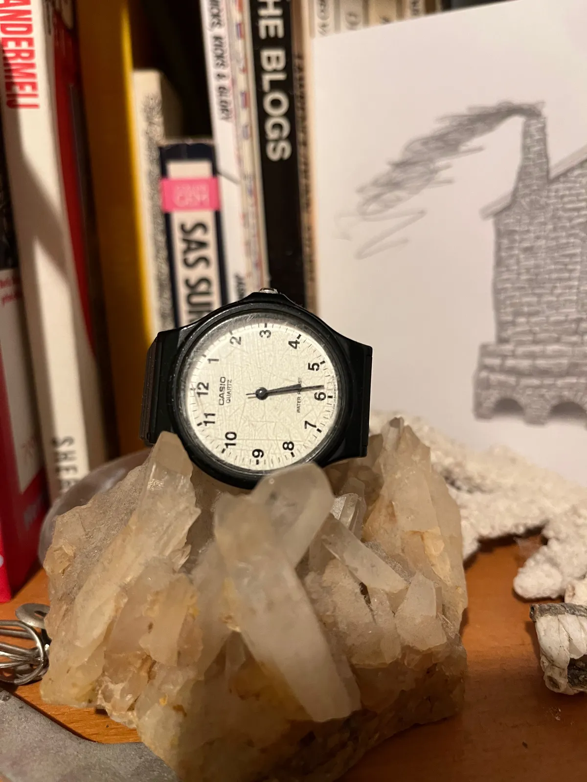 A watch on a rock in front of some books points at 05:28