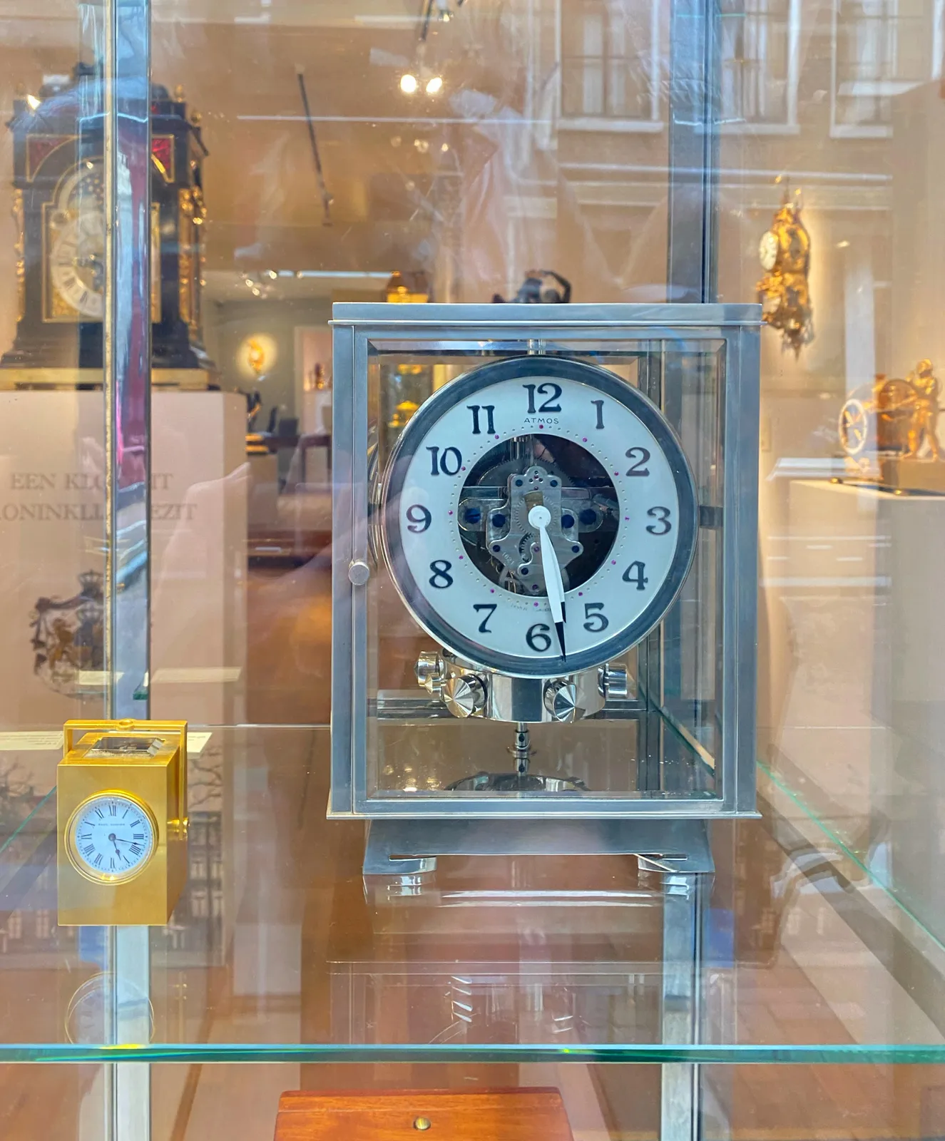 There are quite a few clocks in this picture. It seems to be a clock store. The time can be read on two of them. There’s a small golden one that points at 17 minutes past 5, and there’s a large silver clock that points at 28 past 5.