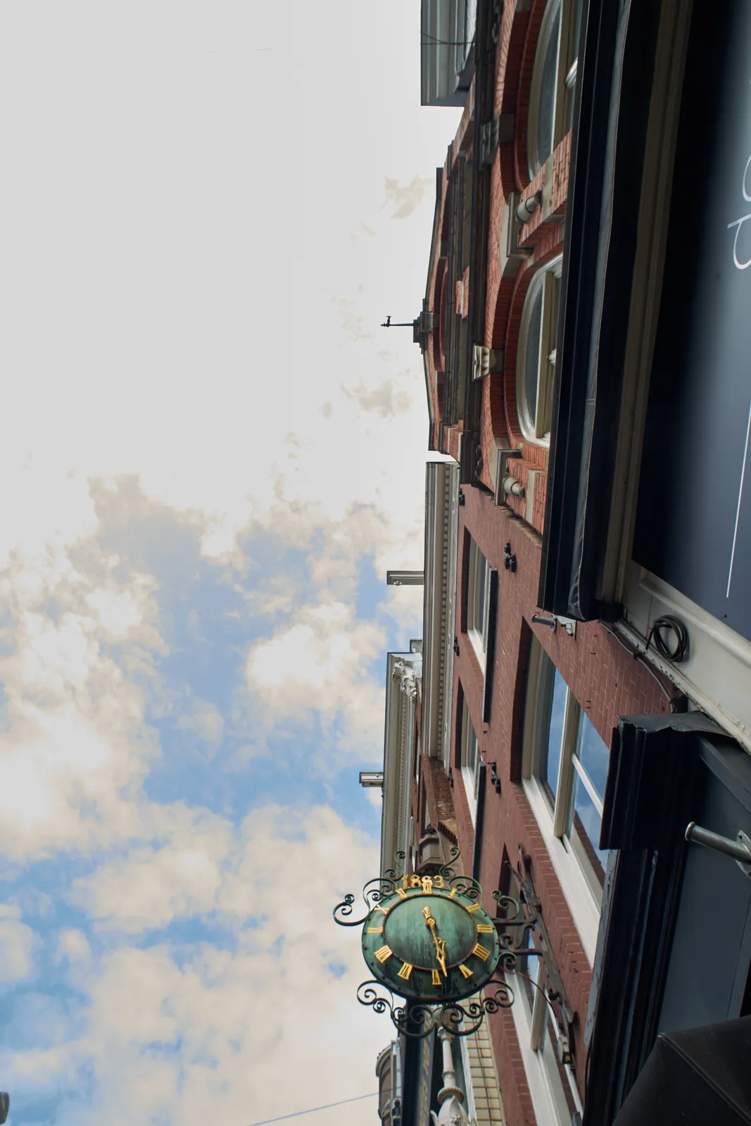 Looking straight up, but in a very wide angle. There’s a very old rather ornamental clock attached to a building. It points at 28 past 5.