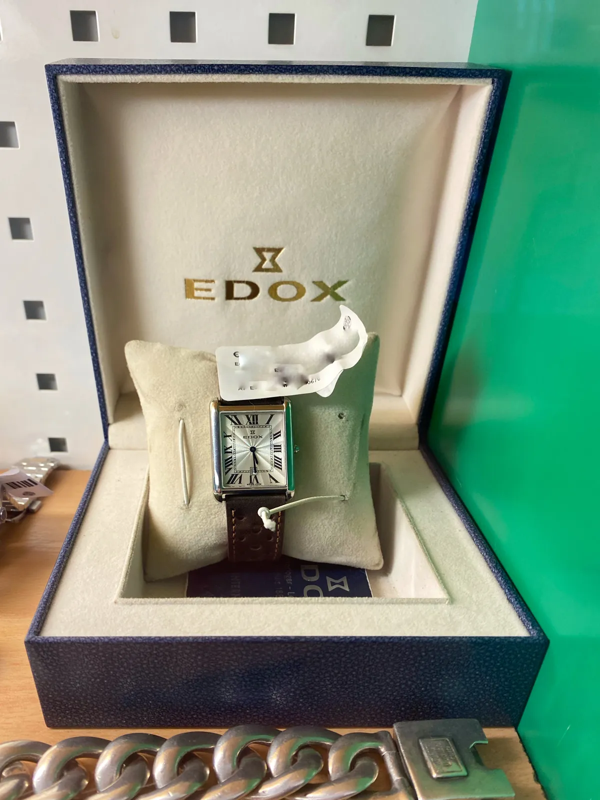 A simple watch in its box. Edox it says on both the box and the watch. It points at approximately 29 minutes past 5.