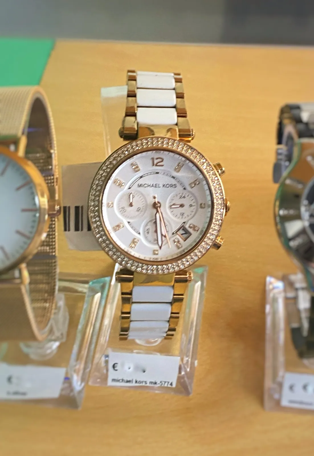A shiny blingbling Michael Kors watch, with diamonds on it. It points at 29 minutes past 5.