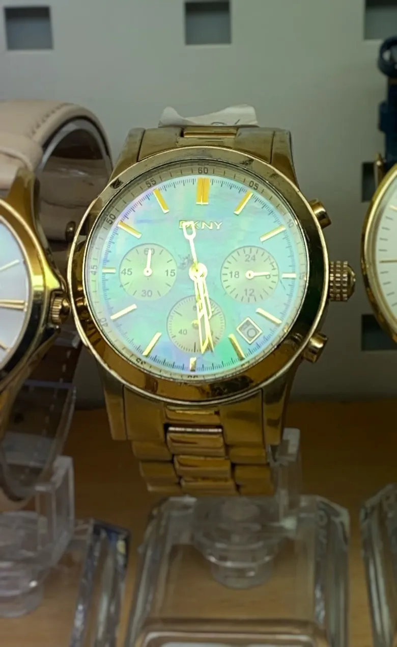 A golden shiny DKNY watch. It points at 29 minutes past 5.
