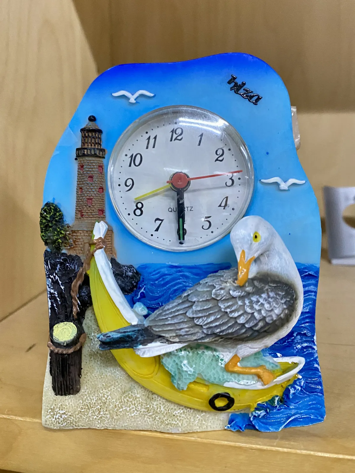 A ceramic thing from Ibiza with a seagull, a lighthouse, a boat and a clock. The clock points at half past 5.