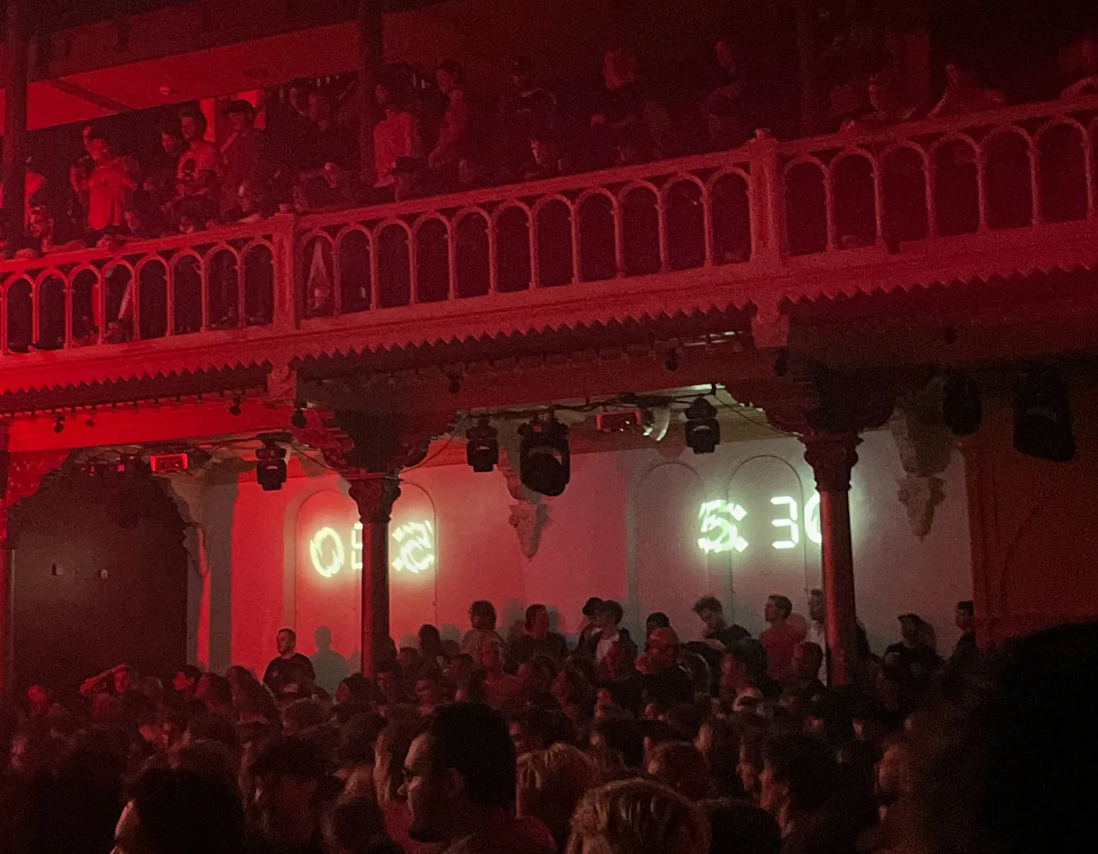 A concert hall with lots of people. On the wall the time stamp 05:30 is projected.