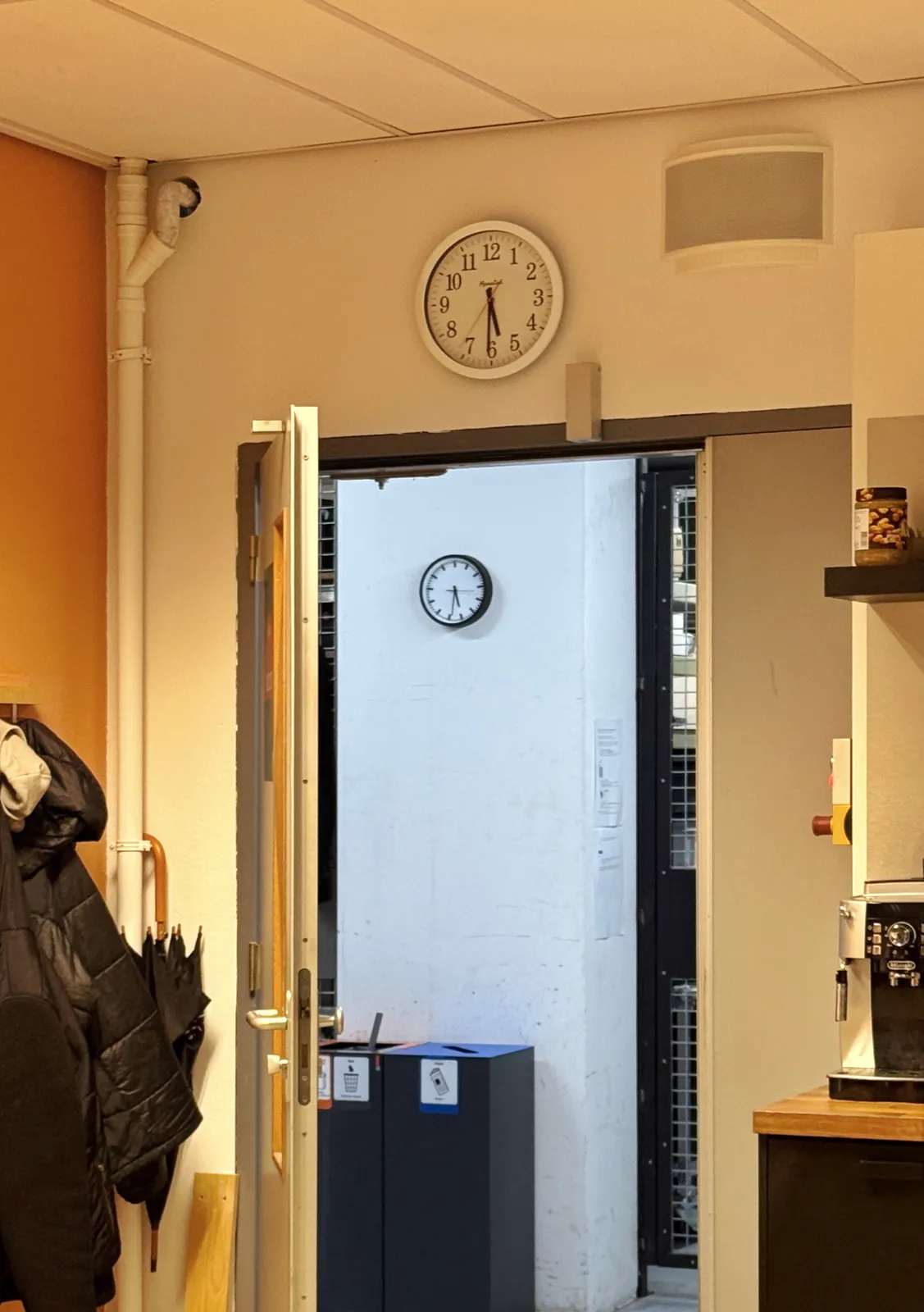 Two clocks. One above a door, the other on the wall behind the door. The one in the back has thriteen hours, instead of the usual twelve. The both point at 31 minutes past five, though on the one in the back this is a bit harder to see. 