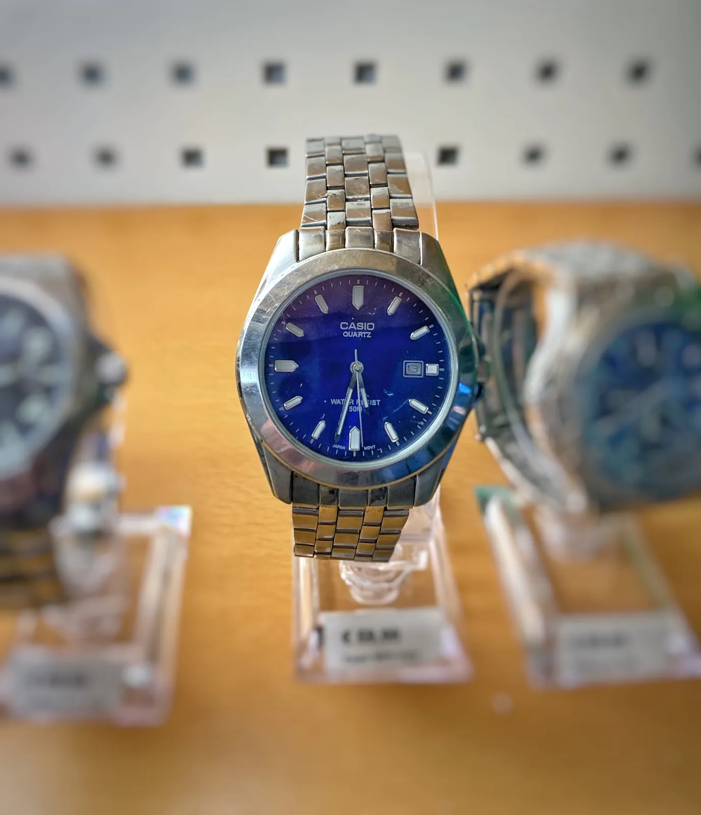 A Casio Quartz watch, with a blue shiny face. It points at 28 minutes to 6.