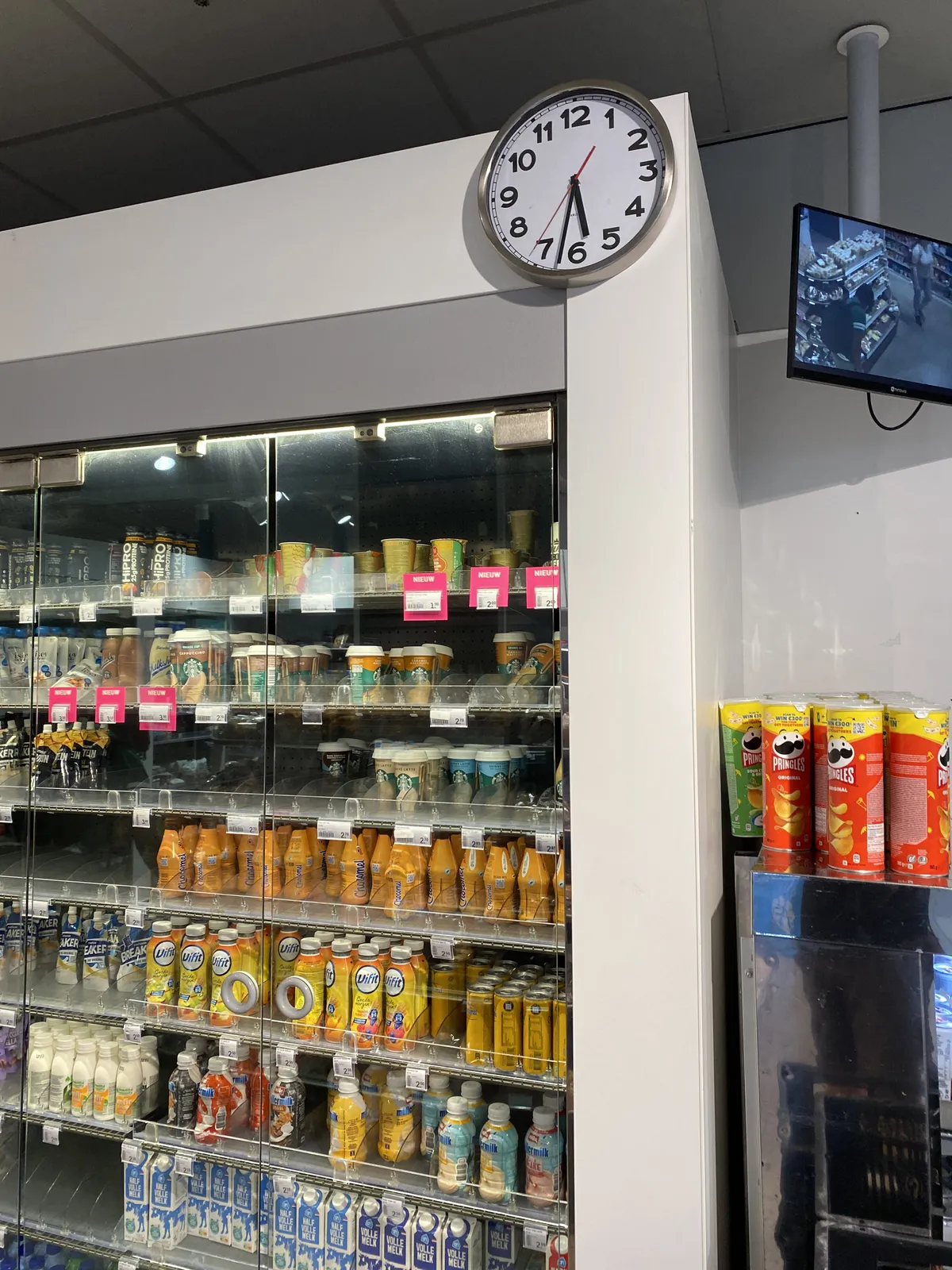 A clock in a shop points at 32 minutes past 5. You can see someone walking on a CCTV screen.