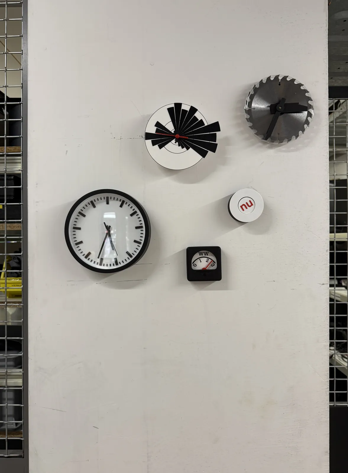 Five works of art on a white wall. Three of them are clocks. One of these clocks looks like a normal station clock, but when you look closely you see that it has 13 hours instead of the usual twelve. You might be tricked into thinking that it points at 36 minutes past five, but it actually points at approximately 32 minutes past five. Then there’s a circular saw with 24 teeth as the face of a clock, which points at approximately 34 minutes past three. And then there‘s a clock with a single red hand which is hard to read. It runs in the opposite direction, and it rotates just once every 24 hours. Once you know that, you can see that it points at approximately 2 minutes to five.