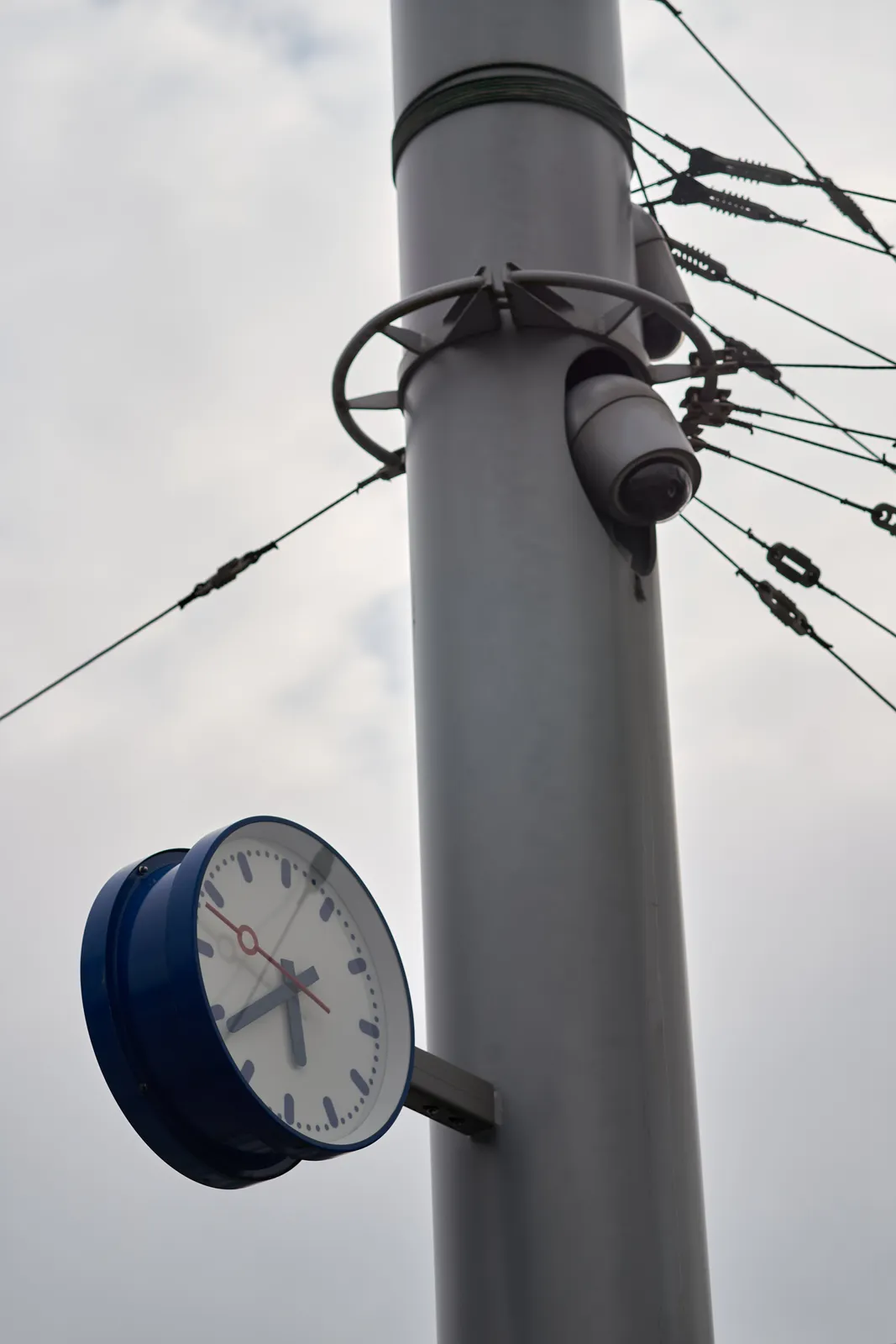 A clock on a pole with many wires attached to it. On the clock it is 39 minutes past 5.
