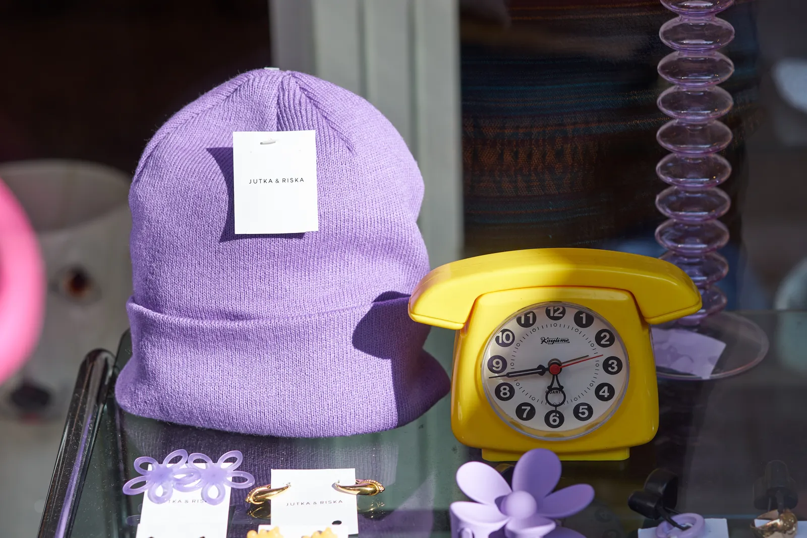 Next to a purple hat in a shop window there’s a yellow clock in the shape of an old rotary phone. It points at 17 minutes to six.