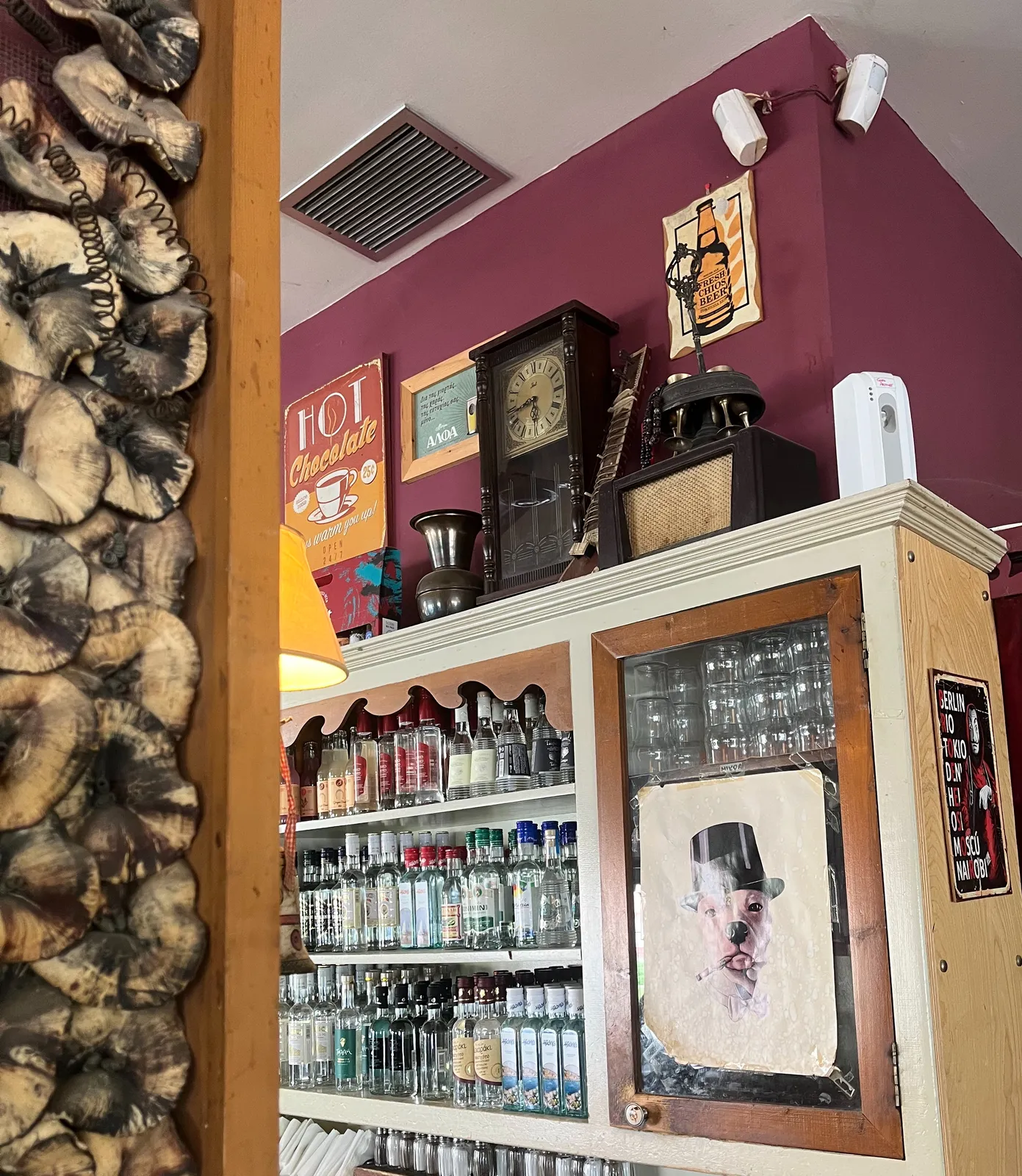 On top of a large closet, filled with all kinds of bottles with alcoholic drinks, next to an old radio and a tiny bouzouki, there’s an old wooden clock. It points at 16 minutes to six.