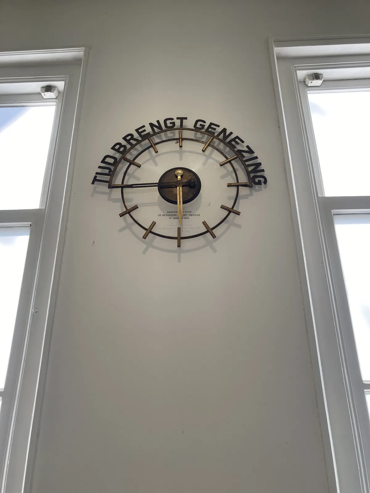 A coper clock, with words around it. They say, translated from Dutch, something like Time Brings Healing. The clock points at 16 minutes to 6.