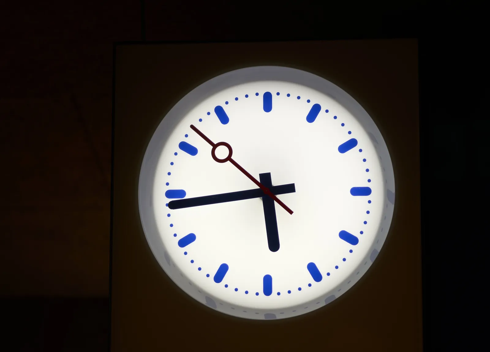 A lit clock with darkness around it points at 16 minutes to 6.