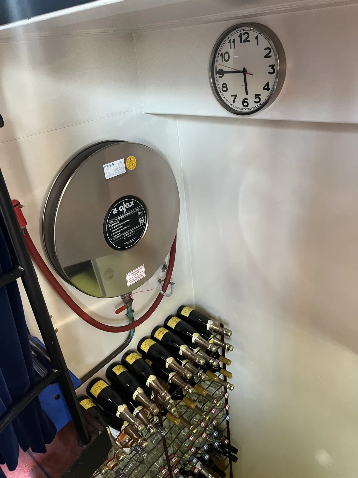 Looking down at a fire hose and a cabinet filled with champaign and other bottles. There’s also a wall clock which points at a quarter to six
