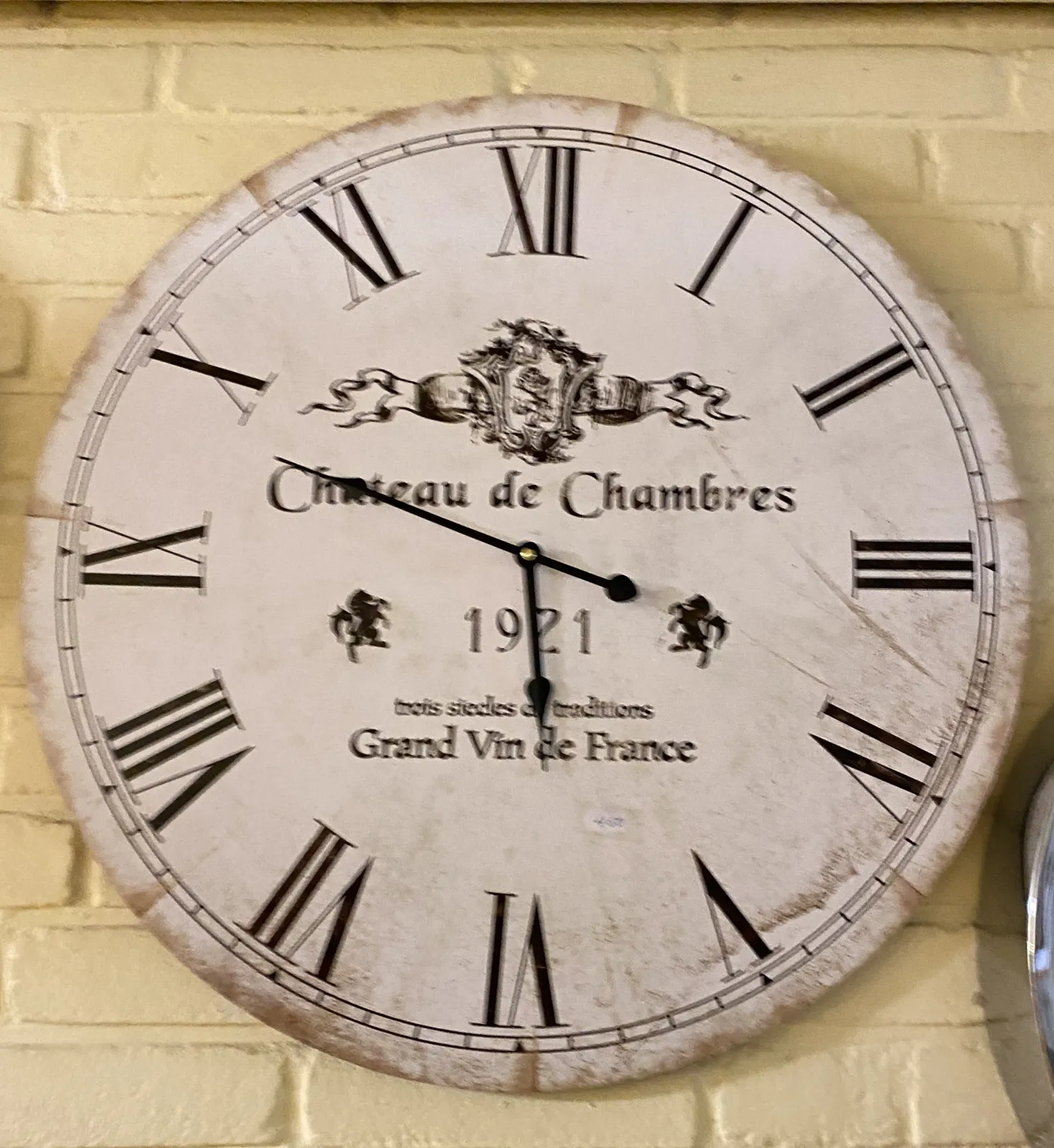 A clock. It has roman numerals. Chateaux de Chambers, Grand Vin de France is printed on its face. It points at 12 minutes to 6.