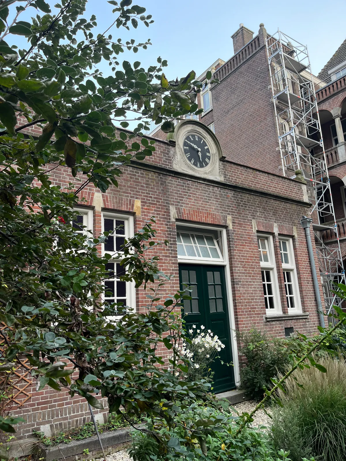 An old brick building with a clock cemented into the wall. It points to ten to 6.