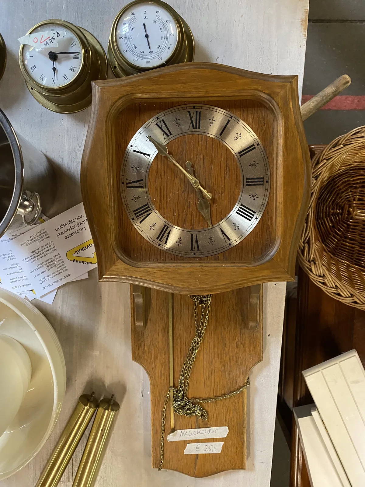 A wooden clock surrounded by stuff in a thrift shop. The hands of the clock point at 8 minutes to 6.