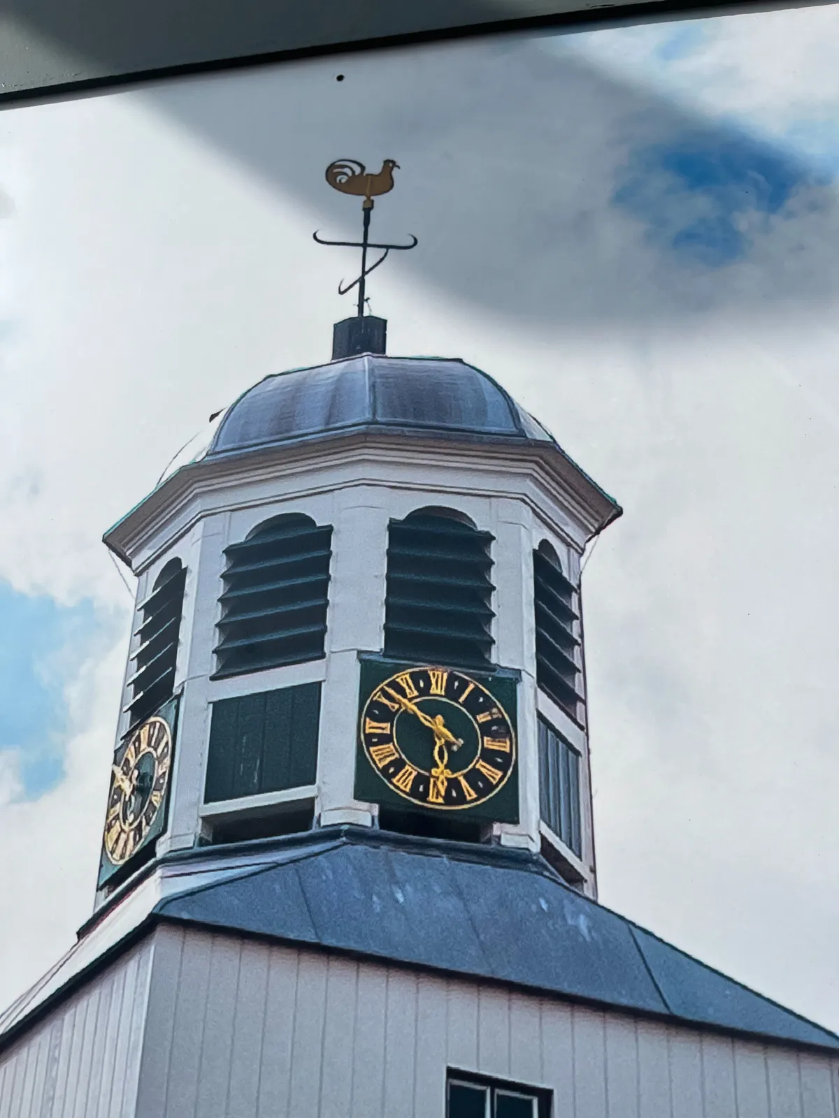 A picture taken from a picture of a small church tower with a clock on it. It points at 8 minutes to 6.