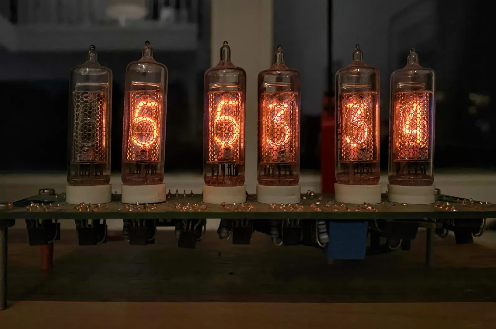 A clock made from glass tubes, with glowing pieces of iron in them. The clock says it is 5 hours, 53 minutes and 34 seconds.