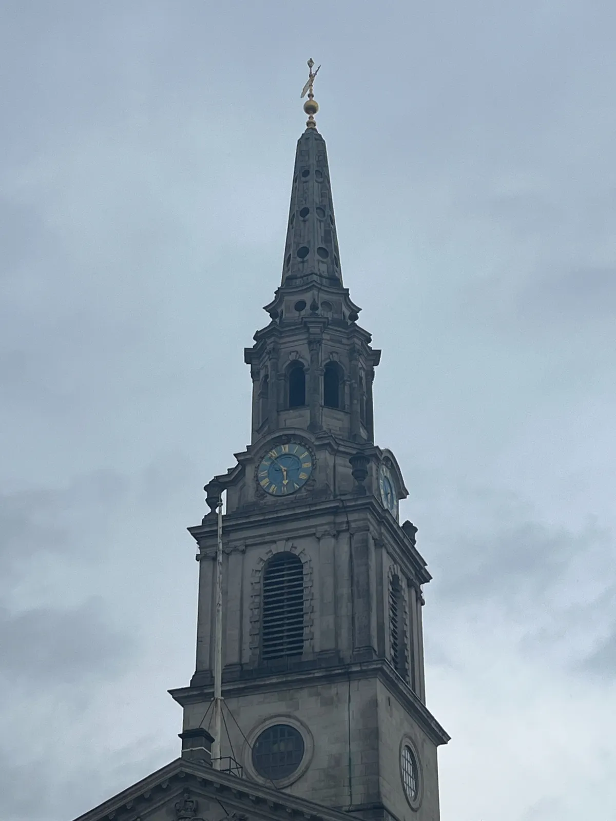 A church tower, with a cloudy, gray sky behind it. The clock on the tower points at 6 minutes to 6.