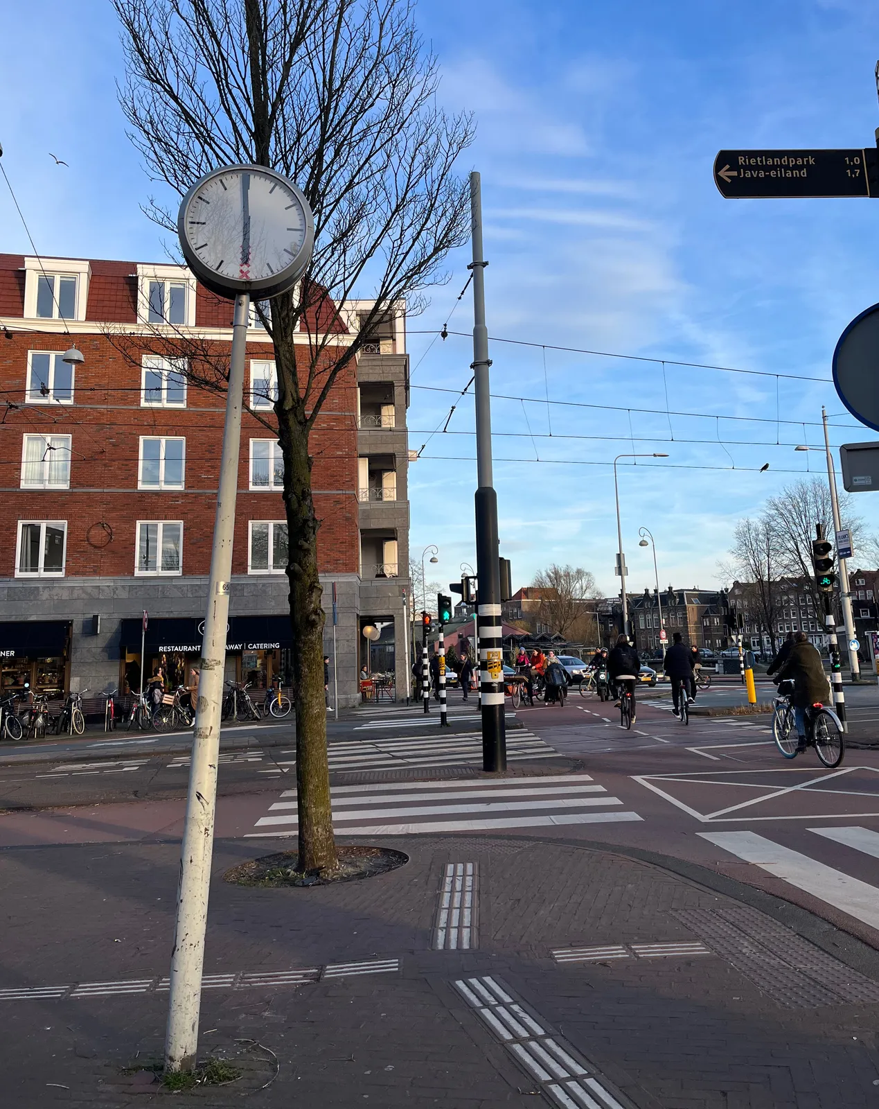 A clock on a pole in Amsterdam points at 1 minute to six.
