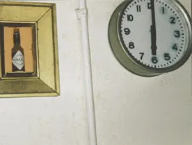 On the left there’s a bottle in an art frame, on the right there’s a clock that points at six o’clock.