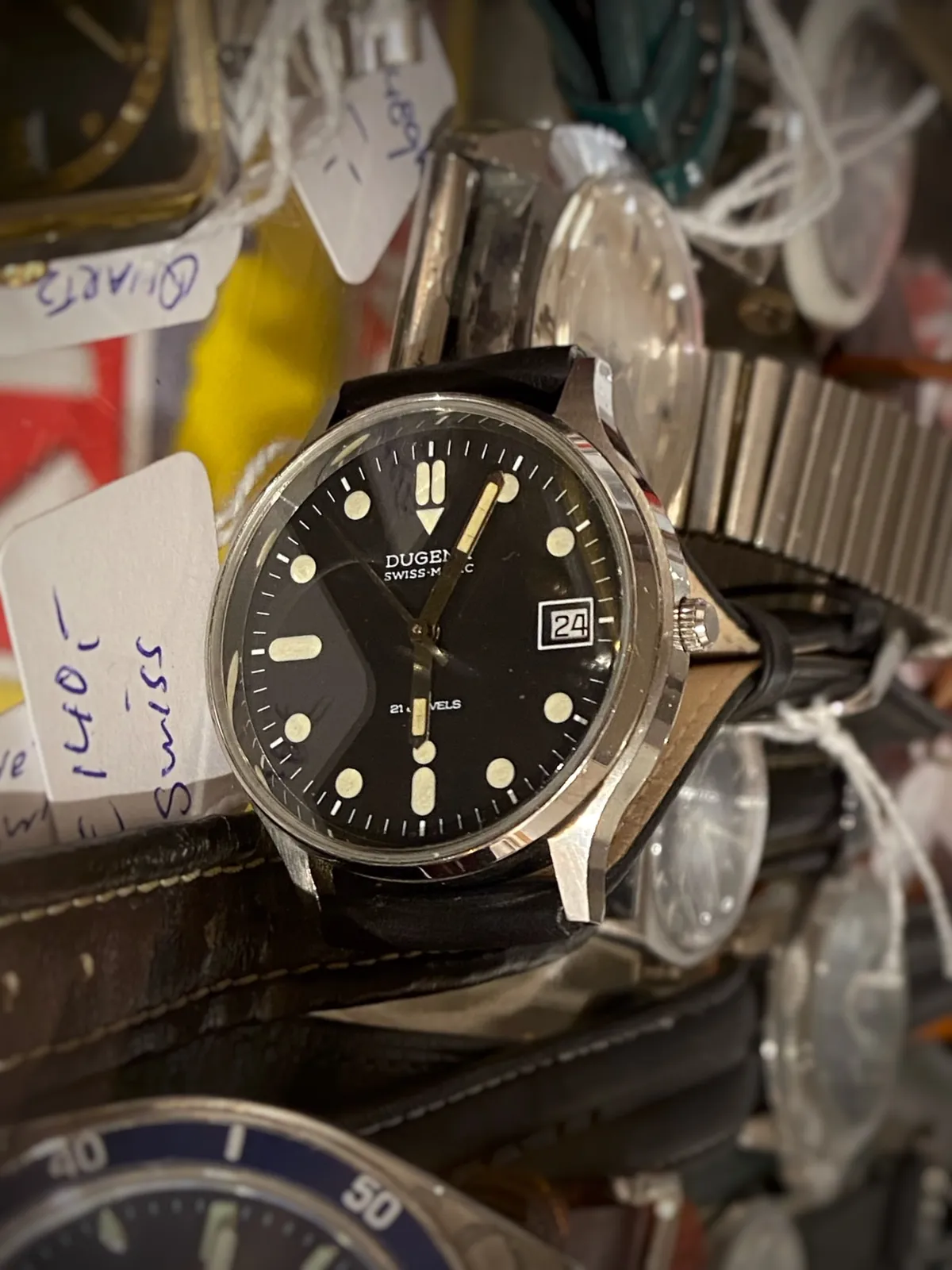 Lots of different wrist watches for sale. A modern one is in focus and it points at 4 minutes past 6.