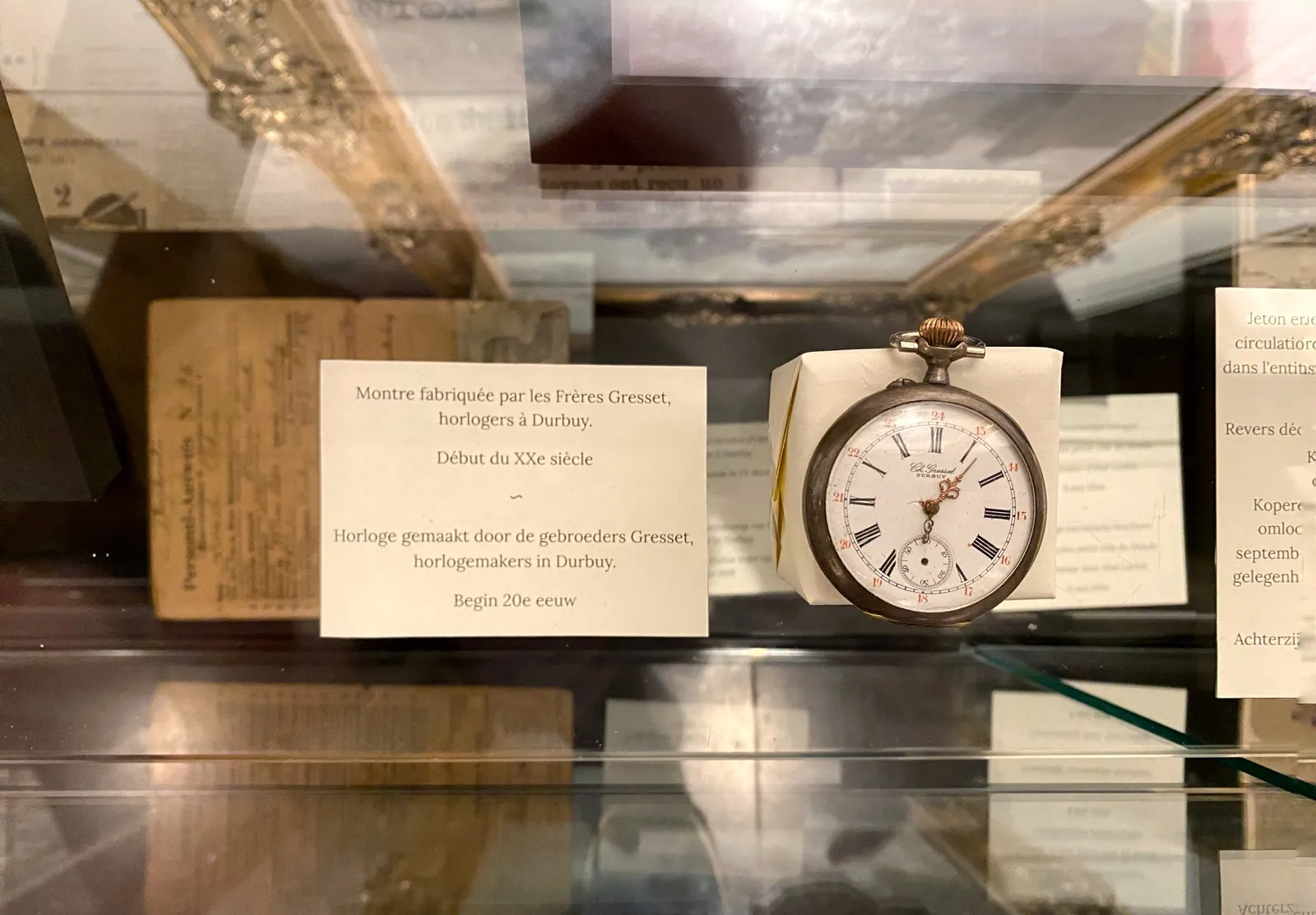 A hand watch. The card next to it says, in French and in Dutch that it was made by the brothers Gresset, watch makers in Durbuy, in the early 20th century. The watch points at 6 minutes past 6, which is pretty accurate for such an old watch.
