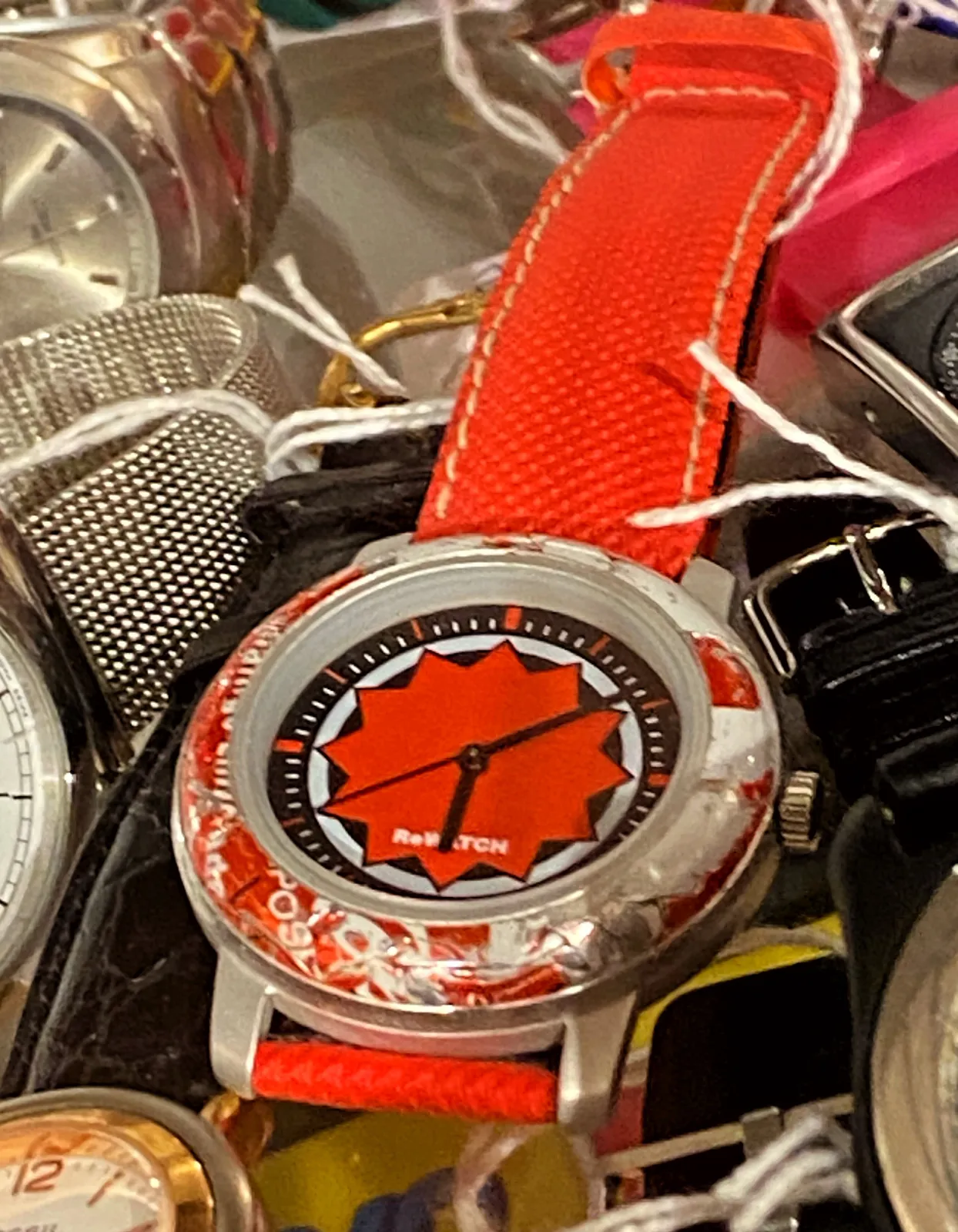 There are quite a few different watches in this picture, but one of them, a bright red one, clearly stands out. It points at 8 minutes past 6.  