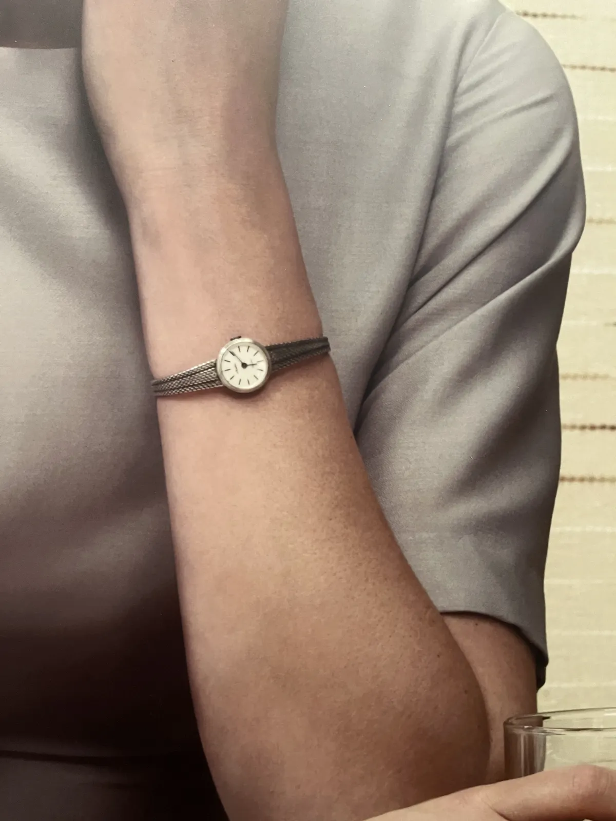 Someone wears a delicate wrist watch. It points at 11 minutes past six.