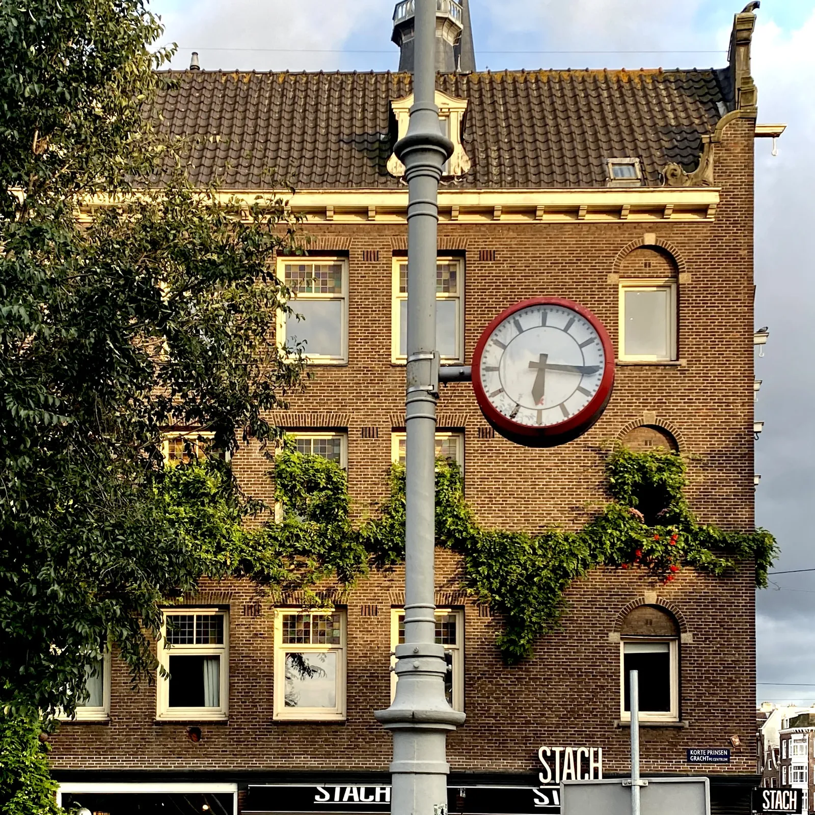 A clock attached to a pole in front of an old, brick building, five stories high. The clock points at a quarter past six.
