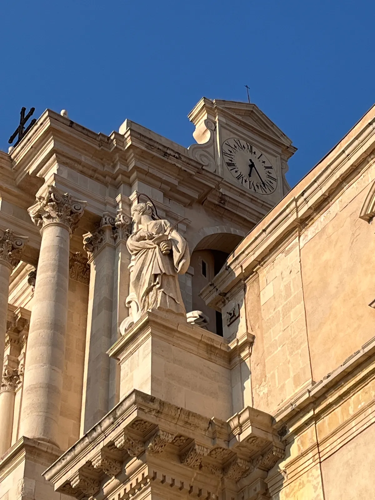 A clock on the side of a very baroque church. It points at 23 minutes past 6.