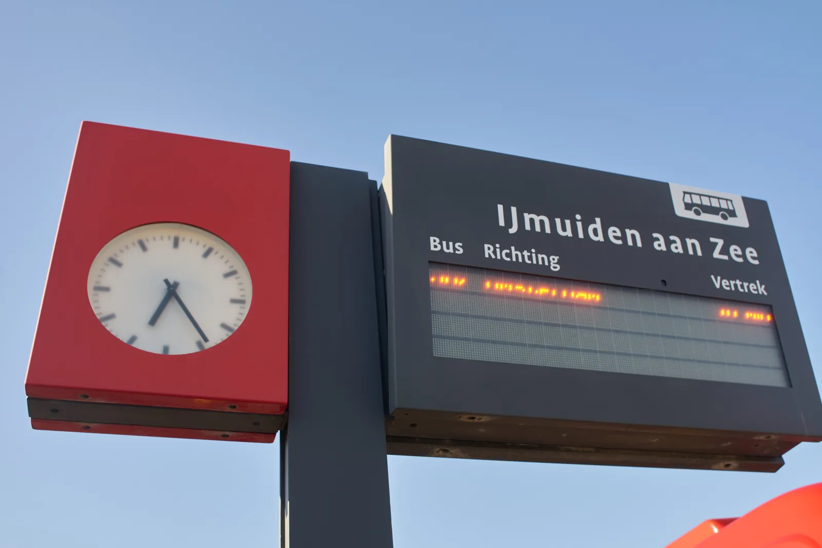 A clock at a bus stop in IJmuiden Beach. It points at 25 past six.