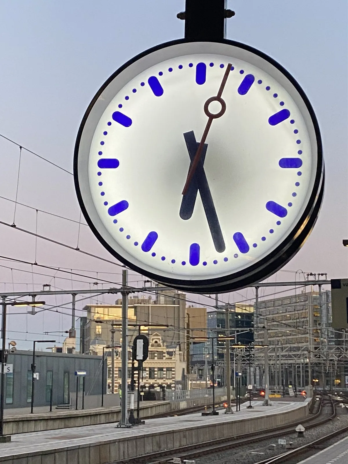 This clock on a platform of a large train station points at 27 past 6.