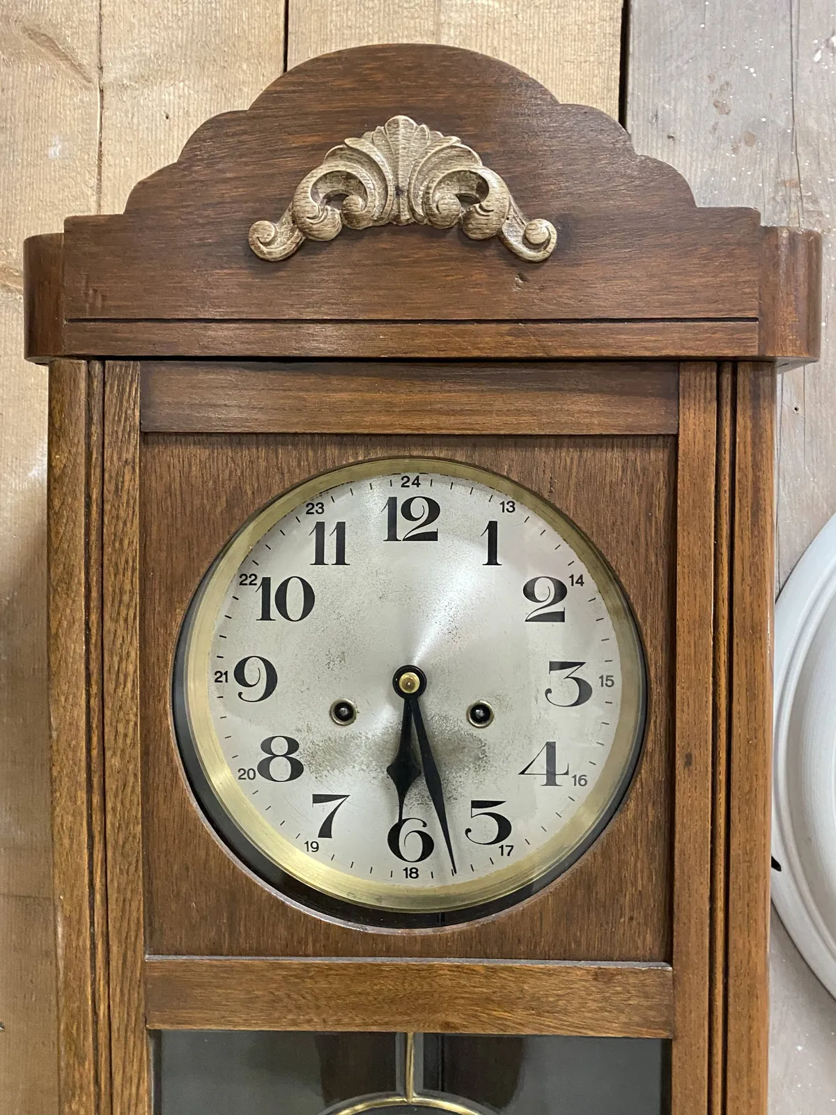 A wooden clock with one simple and modest ornament, points at 27 minutes past 6.
