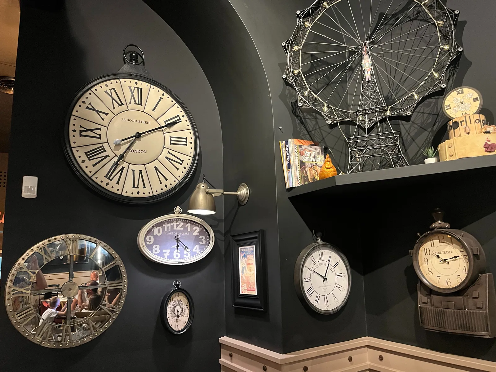 There’s a weird statue made from iron wire which looks like the Eiffel tower with a Ferris wheel attached to it. And there are many clocks. One of the clocks points at 21 minutes past 6. Another one at 29 minutes to 7. There’s a clock that points at 11 past 7, another one that points at 5 past 10, and one that points at 14 past 10.