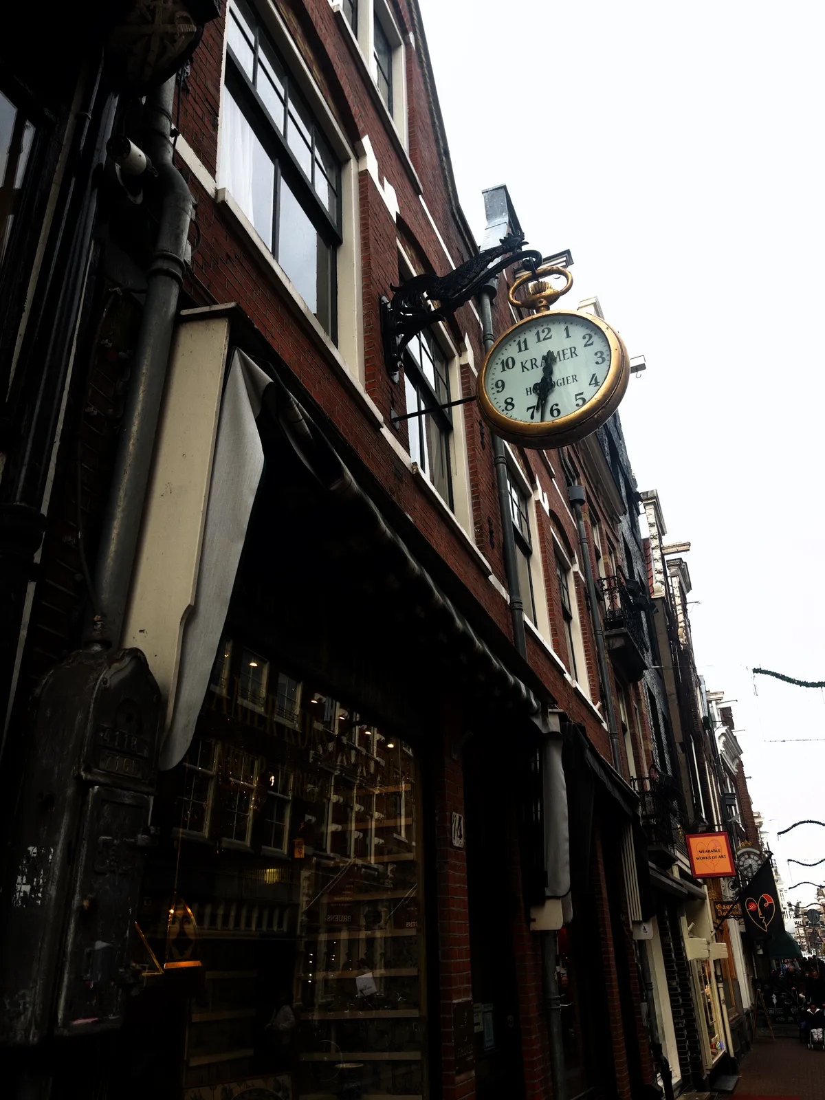 Attached to the facade of a shop in an old shopping street in Amsterdam is this fancy clock, which looks a bit like an old pocket watch. It hangs from a cast iron rooster. The clock points at 32 minutes past six.