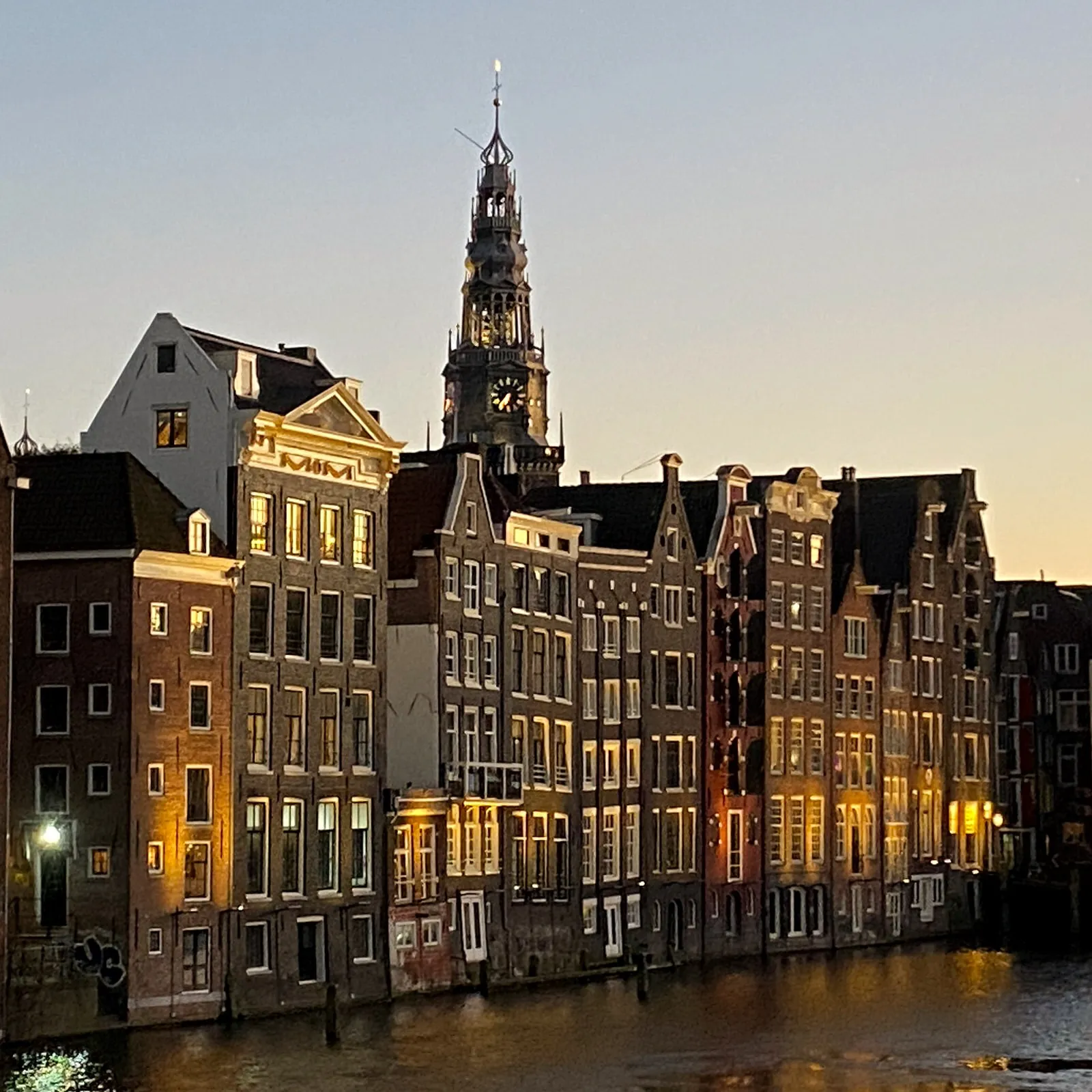 The clock on an old church tower behind some houses on a canal in Amsterdam points at 37 past 6.