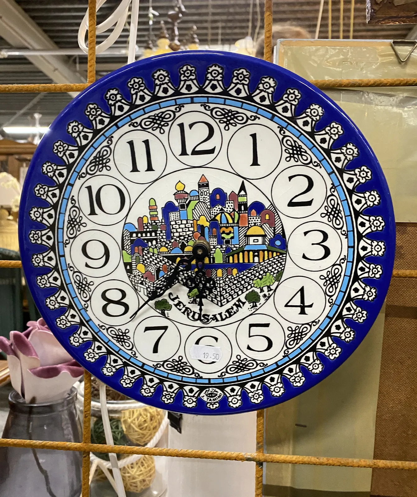 A colourful ceramic plate with houses on it turned into a clock. It points at 22 minutes to 7.