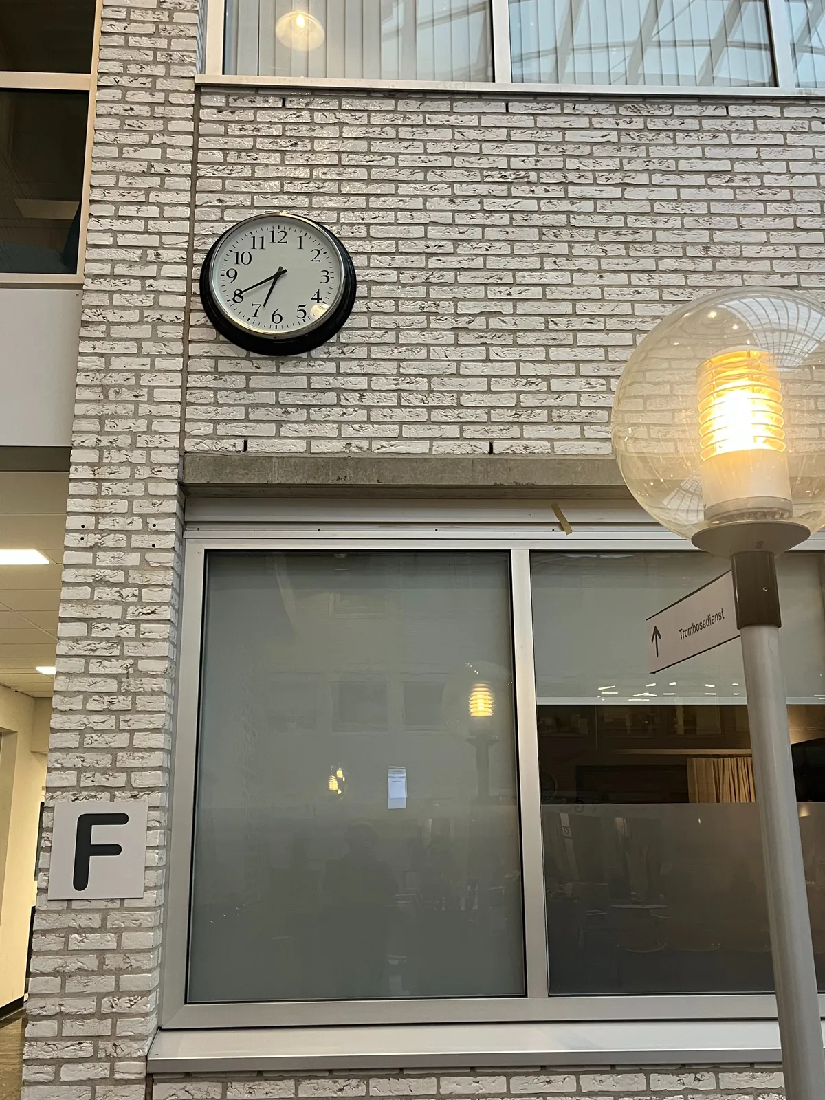 A clock on a gray brick wall. It points at 20 minutes to 7.