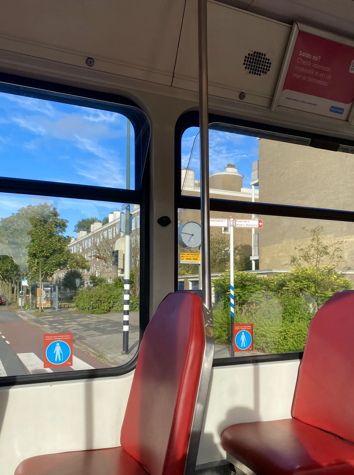 A picture taken from within a bus, or a tram. Outside, in a Dutch town, there’s a clock that points at 14 minutes to 7.
