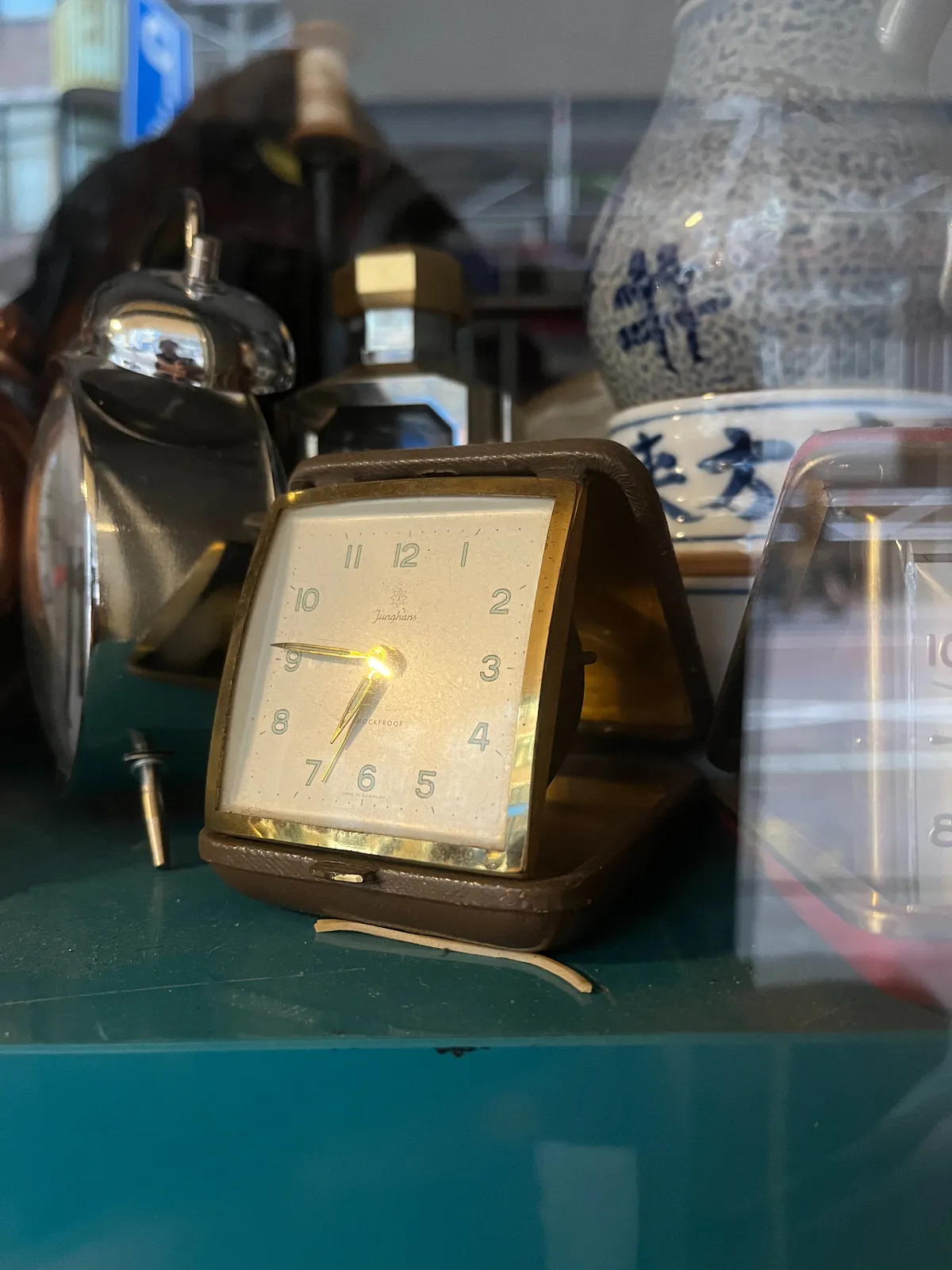 An old, foldable travel clock. It points at 14 minutes to 7.