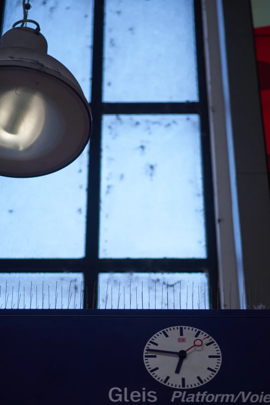 A clock in the Düsseldorf Hauptbahnhof points at 13 to seven. There’s also a lamp and a window in this picture.